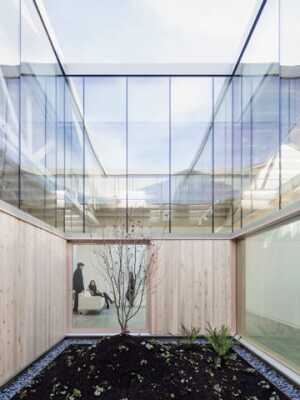 The principal device to bring light into the Bowstring Truss House is a wood- and glass-clad atrium at its center. A large window opens from the living room east of the atrium to overlook the glass walls of the eastern exterior to the garden. Other windows bring light into the office to the west, the kitchen to the north, and the library to the south. (Joshua Jay Elliott)