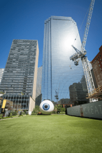 The 30-foot (9.1 m) Eye sculpture by Chicago artist Tony Tasset was installed along Main Street in Dallas. In the background at left stands the 32-story 1600 Pacific building, which was recently redeveloped by HRI Properties as hotel and apartment space; to the right is the 50-story Thanksgiving Tower. (© Hall Group)