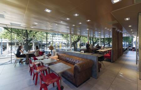 The mullionless glass walls on the east, south, and portions of the west and north walls flood the interior with daylight and integrate the private and public spaces. Interior furnishings add highlights of color. Red Eames molded plywood chairs pull up to pedestal tables anchored to the floor. Black-and-white molded fiberglass chairs complement them. Red banquettes and tufted brown leather sofas vary the mix of seating. (JeroenMusch)